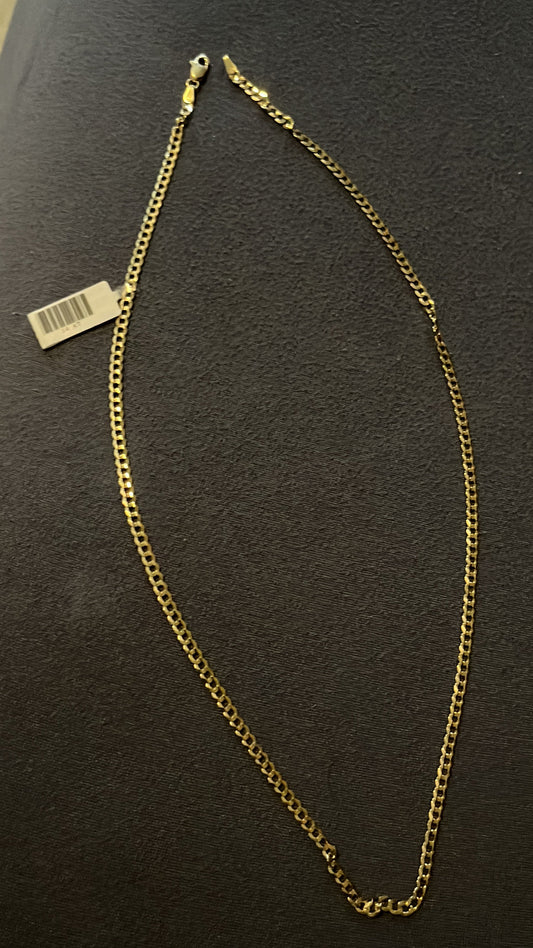 A gold-colored chain necklace with a tag attached, laid out on a textured surface.